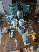 Overview of various items on table including thermoses, Pyrex bowls, ceramic mugs, basket and personal care items