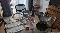 Photo of the table showing holiday-themed round plates, two rectangular holiday serving plates, large metal strainer, vintage wood table lamp with bulb and visible repair, and black frying pan with handle.