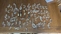 Overhead view showing the full assortment of clear glass or crystal lamp and chandelier prisms arranged on a wooden table, along with a few metal and fabric-covered lamp socket parts.
