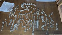 Wide view of assorted chandelier lamp prisms spread out on a wood table, showing a variety of shapes and sizes including drop and round beads