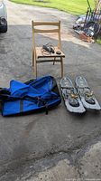 Blue wheeled duffle bag, pair of metal snowshoes with bindings, jump rope, and hockey puck arranged on ground next to chair.