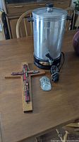 Wide view of wooden cross with colorful tile inlays, 35 cup aluminum percolator with indicator light, and small ceramic holy water font