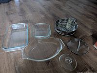 Three Pyrex glass casserole dishes, one stainless steel strainer, and two glass lids displayed on floor.