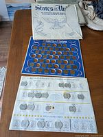 Overview of the blue display folder laid flat with coin slots, white outer cover above, and part of a shoe visible nearby