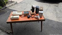 Wide view showing two vintage bakelite intercom units, plug-in heat lamps, cords, and a wood table.