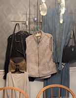 Photo showing hanging clothing items including a black jacket, fuzzy vest, denim jacket, and two purses.