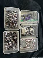 Top view of five clear plastic containers filled with black and assorted color freshwater pearls in various shapes and sizes, some strung together.