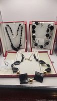Three black necklaces displayed in boxes showing their bead details and closures.