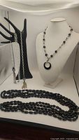 View of all jewelry pieces displayed together showing the onyx pendant necklace, the open silver necklace with tassels on a hand display, and the black onyx bead strands.