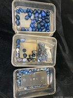 Top-view of clear plastic containers holding mixed polished stone beads with various shades of blue, including some in plastic baggies.