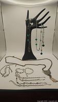 Glass beads and crystal long necklace draped on black hand display, two silver rope bracelets and leopard pendant necklace laid flat