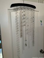 Photo of 11 long chain necklaces hanging from a black plastic multi-hook hanger on a white door. Some chains have decorative station beads.