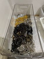 Clear plastic container with assorted chains in black, silver tone, gold tone, and brown colors packed together.