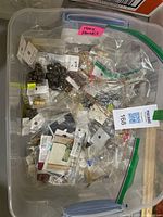 Clear plastic storage bin filled with multiple small plastic bags containing various packaged costume jewellery findings for jewellery making, including chains, beads, and clasps.