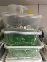Top view of stacked clear plastic containers with various colored crystal beads visible inside, including green and iridescent beads.