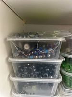 Top three stacked plastic storage bins filled with assorted crystal beads of blue, black, and clear colors and some in plastic bags