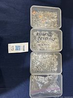 Four stacked plastic containers filled with various clear and some iridescent crystals including Swarovski and rock crystals.