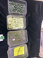Four trays containing various green gemstone beads: dark green faceted ruby zoisite beads on a string, pale green tumbled chrysoprase beads, small green emerald chips, and a collection of strung green quartz beads.