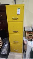Front view of the yellow 4-drawer filing cabinet showing four drawers with silver handles and a price tag attached.