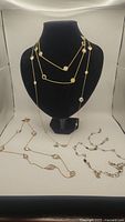 Four gold filled chain necklaces with varied crystals and gemstones displayed on black bust and white surface