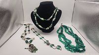 Four green necklaces displayed together showing variety of beads and pendants