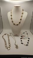 Four necklaces displayed on white bust and flat surface showing chain styles and bead details