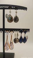 Front view of four pairs of earrings displayed on black stand including faceted labradorite, cubic zirconia, smoky quartz, and blue cloisonné vintage style earring pairs
