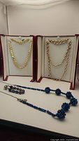Photo of two gold plated hammered texture necklaces displayed in boxes and blue crystal bead necklace and matching bracelet with sterling silver chain below.