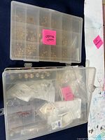 Two plastic compartment boxes containing assorted gold filled jewelry findings including beads, jump rings, clasps, and eye hooks.