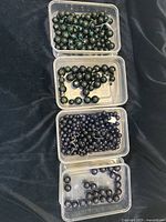 Four plastic containers holding faceted round Goldstone beads in green and blue colors in various quantities and sizes.