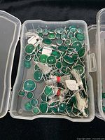 Clear plastic box containing multiple green onyx stones set in silver and gold bezels, various shapes and sizes mostly round and cushion cut.
