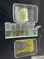Overall view of compartments filled with different sizes and shades of green jade beads, plus a plastic container of yellow-green round beads.
