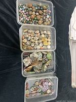 Four clear containers filled with assorted Jasper and Agate stones and beads in varied shapes and earthy colors on a black fabric background.