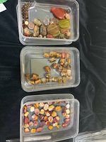 Three plastic containers with mixed polished stones of varied colors and sizes including jasper and quartz.
