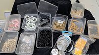 Wide view of twelve plastic cases containing assorted beads, spools of craft wire, and a bag of needles arranged on a black cloth.