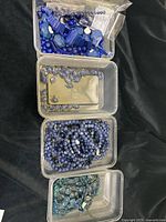 Top view of four plastic containers holding various beads including lapis lazuli, kyanite, sodalite, and apatite beads.