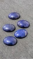 Five polished lapis lazuli stones arranged on black fabric under natural light showing blue color and flecks.