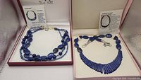 Two lapis lazuli bead necklaces in presentation boxes. Left: multi-strand with oval and round beads and gold details. Right: lapis strip fan necklace with silver chain.