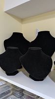 Four black velvet necklace display busts on a white shelf, two large and two small sized busts grouped together.