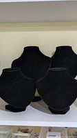 Front view of two large and two small black velvet necklace display busts arranged on white shelf.
