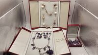 Overview of the lot showing pearl bead necklace on top, amethyst necklace set on left, and earrings on right in boxes.