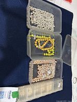 Plastic containers with assorted freshwater pearl strands and loose pearls in various colors and sizes on dark fabric.