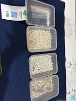 Four clear plastic containers holding loose white and cream freshwater pearls in various sizes and shapes