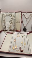 Overview of four necklaces in presentation boxes: silver plated link necklace, sterling silver snake chain with druzy pendant, gold and silver tone necklace with colored pendants, silver chain with crystals.
