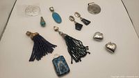 Full assortment of eleven silver pendants and earrings featuring beaded tassels and stone drops on white background.