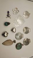 All twelve pendants arranged flat showing variety in designs, stones, and metals.