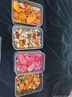 Four plastic containers filled with various colors and shapes of turquoise and jasper beads on a black fabric background.