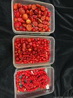 Top view of three plastic containers filled with beads and coral chips of various shapes and sizes. The first container has larger irregular red coral beads, the second with small cylindrical and round bamboo coral beads, the third with strings and loose red beads.