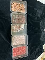Five containers filled with different types of quartz beads including tumbled stones, chips, and bezel-set beads.