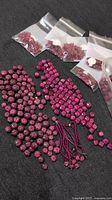 Overview of multiple ruby gemstone beads including loose and bagged beads, faceted cube-shaped and carved round beads on black surface with 10 cent coin for scale.